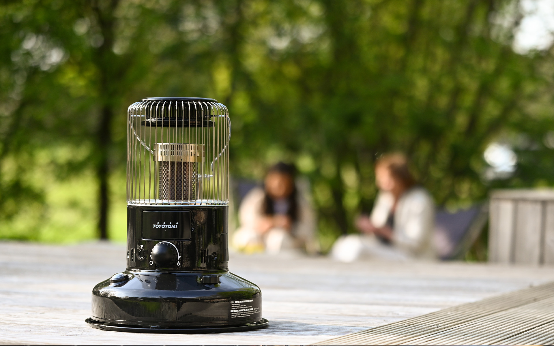 Toyotomi KS-R26 round heater placed on a patio with people enjoying outdoor warmth in the background