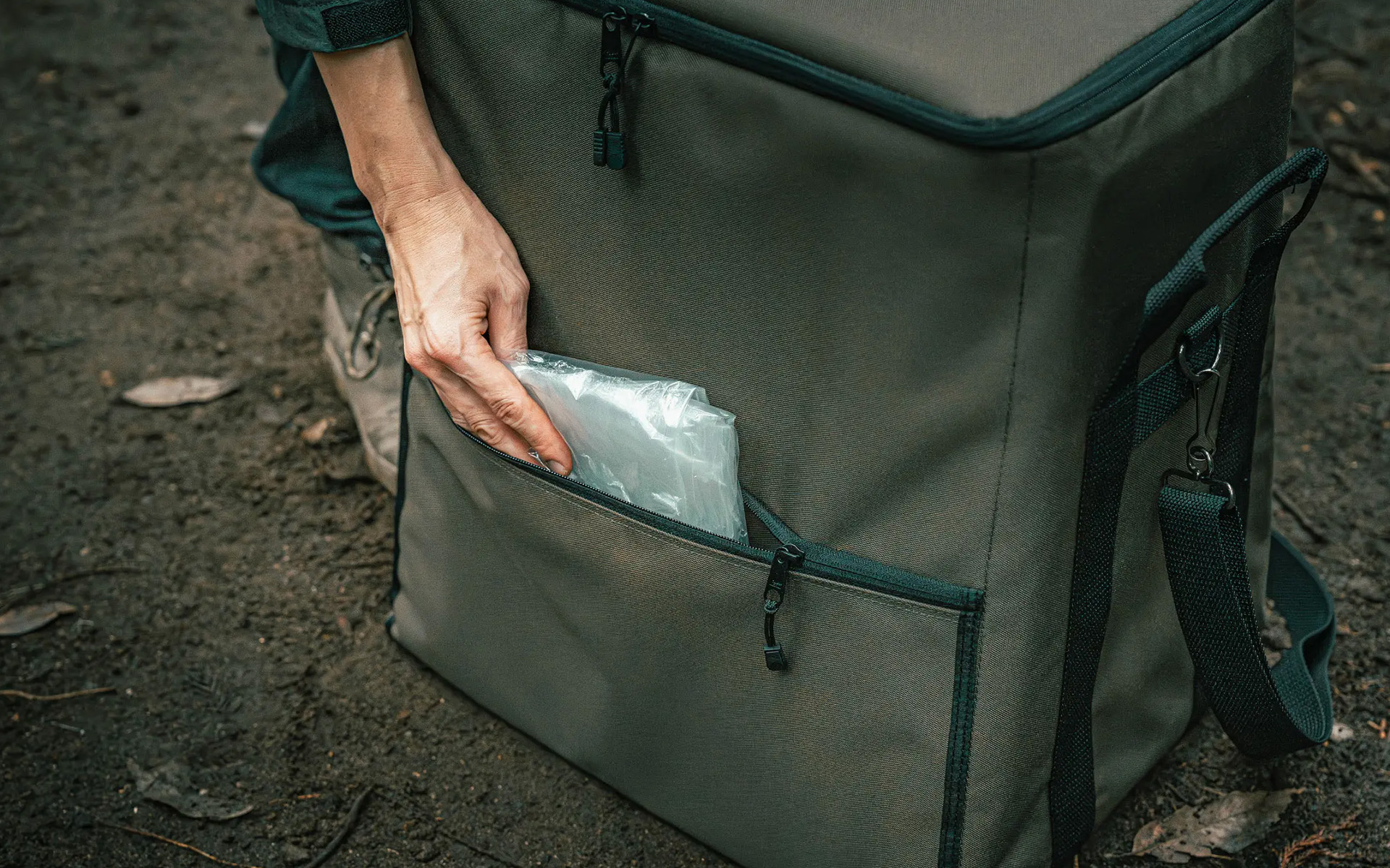 Toyotomi GEAR MISSION bag’s rear extra storage pocket being filled with a plastic bag, showcasing additional carrying capacity.