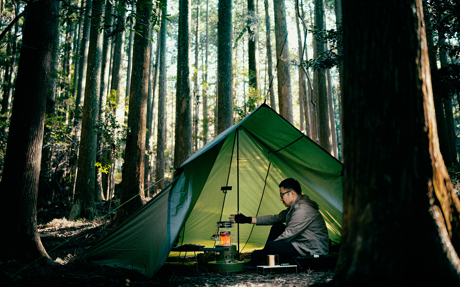 Toyotomi GEAR MISSION round heater warming a person inside a tent set up in a large forest.