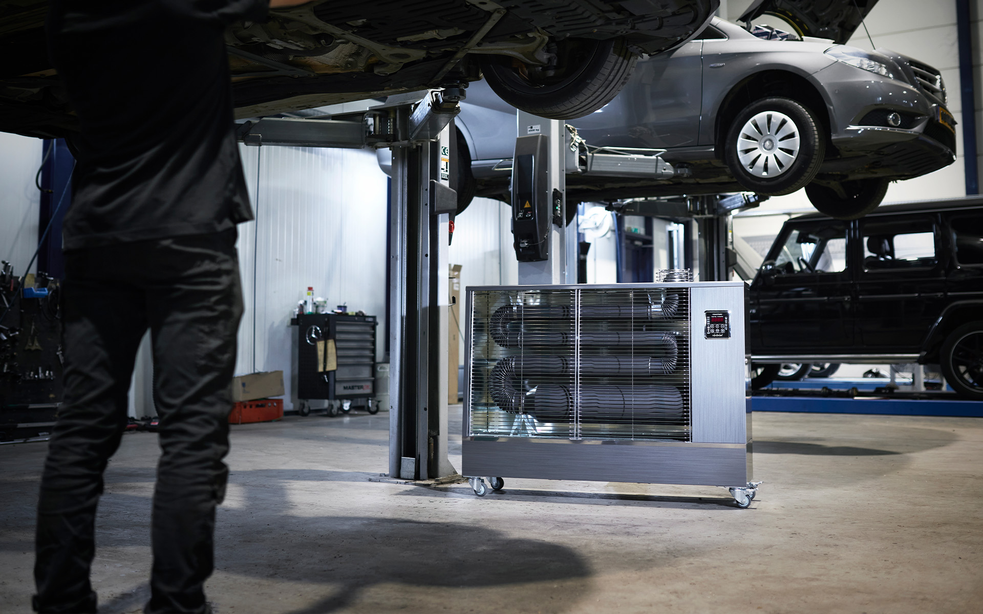Toyotomi Infrared Heater TIB-16 warming a mechanic working on a car inside a garage, delivering efficient and focused heat.