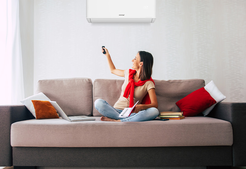 Una mujer en un sofá encendiendo el aire acondicionado Toyotomi SORA para disfrutar de aire fresco y una sala de estar confortable.