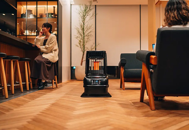 Estufa de parafina Toyotomi en medio del vestíbulo de un hotel con 2 personas disfrutando del ambiente confortable y acogedor