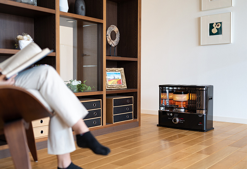 Toyotomi wick heater in living room with a girl reading a book on a chair being warmed up by the paraffin heater, Zibro branded heater