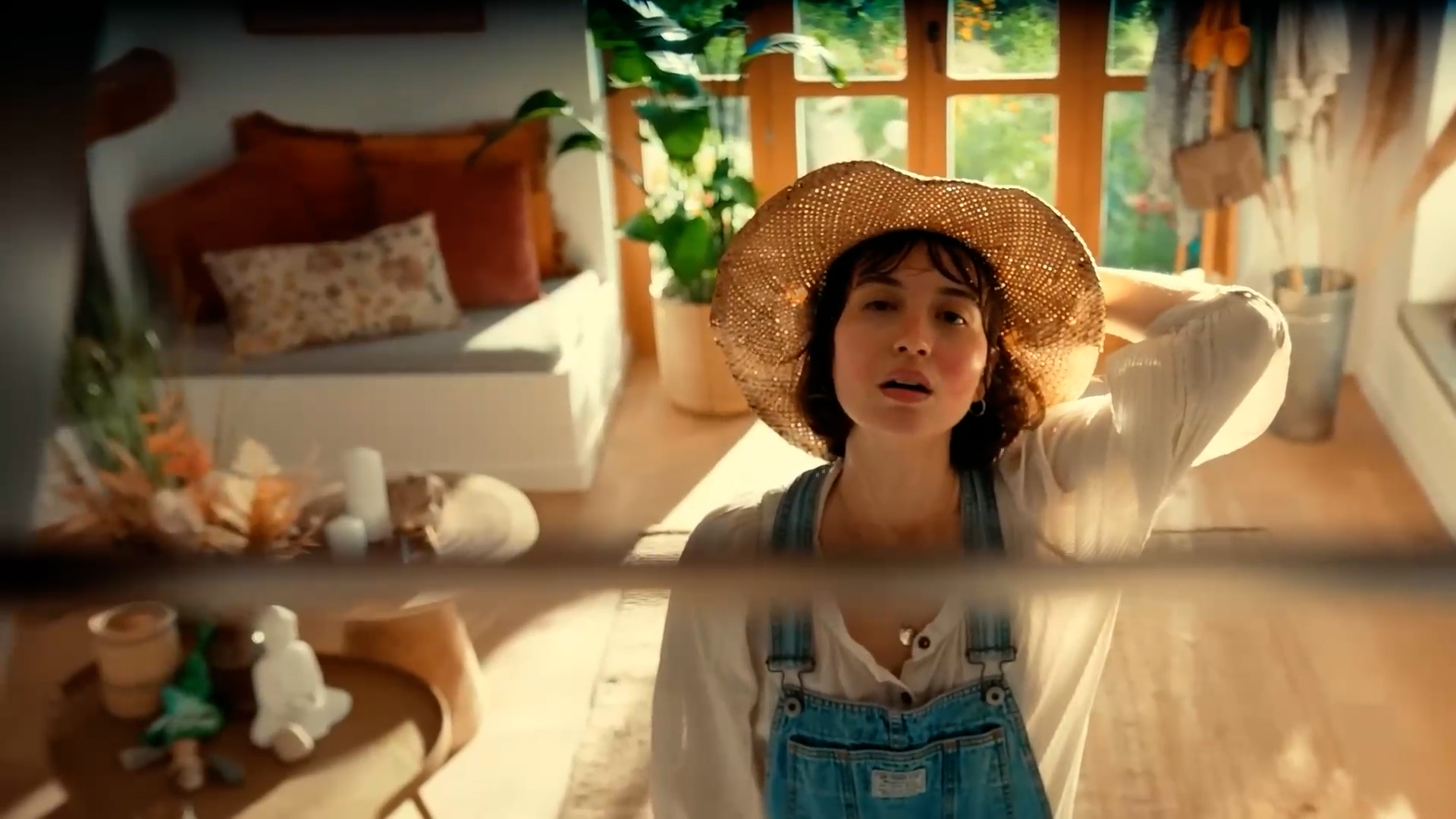 Lyst, indbydende indendørsrum med en kvinde iført en stråhat, naturligt lys og hyggelige møbler, perfekt til en afslappende hjemmeatmosfære.