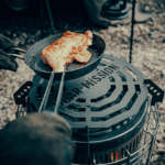 Close-up of chicken being grilled on a portable barbecue grill outdoors.
